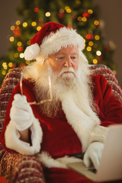 Santa sosteniendo sus gafas y usando la computadora portátil