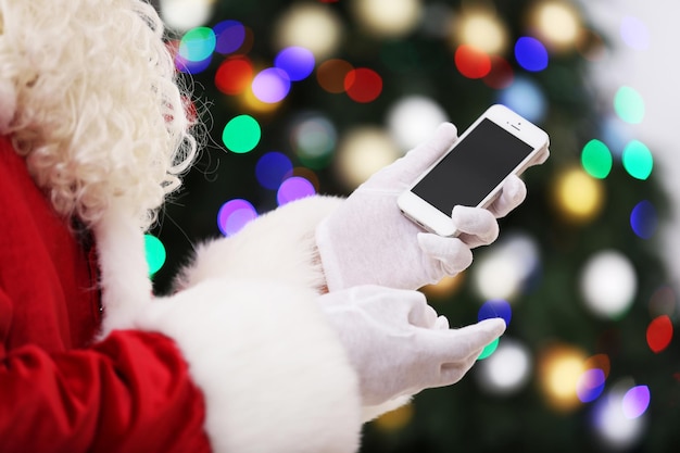 Santa sosteniendo el teléfono móvil en el fondo del árbol de Navidad