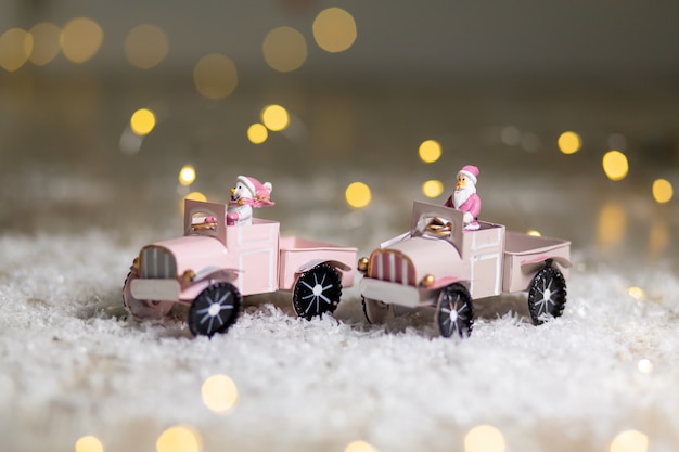 Santa Statuette fährt auf einem Spielzeugauto mit einem Anhänger für Geschenke Festliches Dekor, warme Bokeh Lichter.