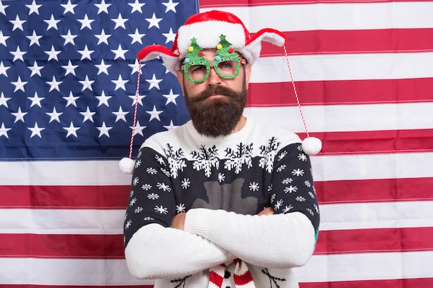 Santa te está mirando. El hombre barbudo usa gafas divertidas. Hipster divertido en el fondo de la bandera americana. Divertido pero patriótico. Diversión de invierno. Feliz Navidad. Divertida idea de disfraz de año nuevo. Celebración navideña.