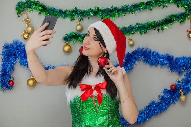 Santas sexy Helferin Leidenschaftliche Brünette in einem Elfenkostüm mit einem Telefon in der Hand