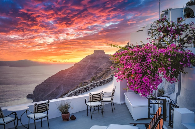 Santorini Grécia Cenário de viagem deslumbrante com cadeiras de flores cor de rosa terraço ensolarado céu azul Romance