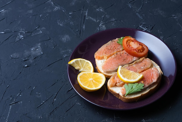 Foto sanwiches abiertos con pan y salmón ahumado, tomates sobre fondo oscuro