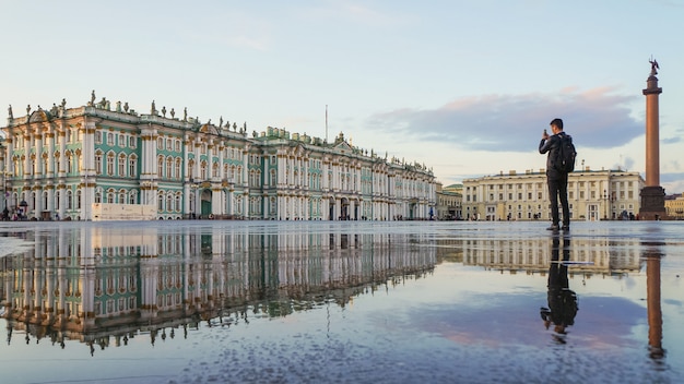 São Petersburgo. Turista na praça do palácio leva ao telefone o Museu Hermitage.