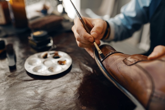 Foto sapateiro com pintura a pincel, serviço de reparação de calçado. habilidade do artesão, oficina de calçados, obras-primas com botas, sapateiro