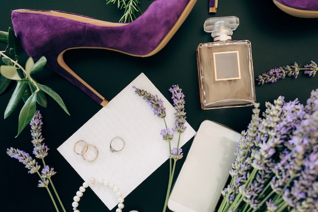 Sapato de salto alto lilás um frasco de perfume uma joia para smartphone e flores em uma superfície verde