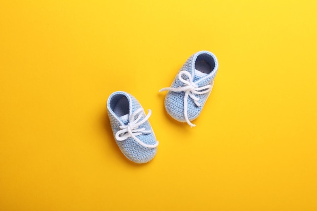 Sapatos de bebê de malha azul sobre fundo amarelo, vista de cima, espaço de cópia plana