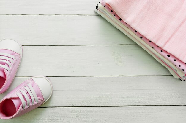 Sapatos de bebê rosa menina e roupas recém-nascidas. conceito de maternidade, educação ou gravidez com espaço de cópia. configuração plana.