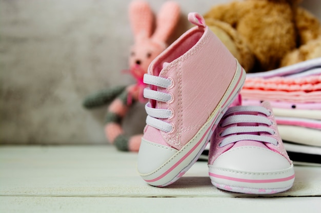 Sapatos de bebê rosa menina, roupas para recém-nascidos e brinquedos macios. Conceito de maternidade, educação ou gravidez com espaço de cópia.