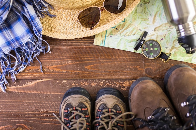 Sapatos de caminhada com mapa topográfico e bússola em um fundo de madeira.