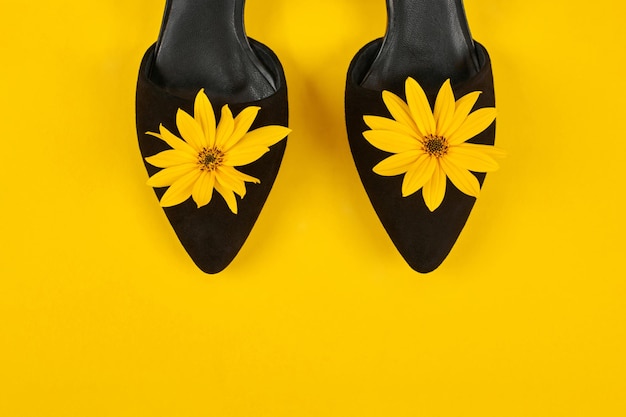 Sapatos de corte preto de camurça com botão de flor de topinambur amarelo no conceito de feminilidade de fundo amarelo