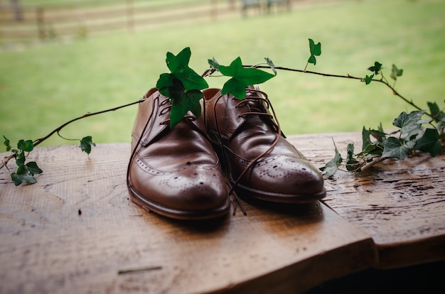 Sapatos de noivo elegante marrom lindo em uma mesa de madeira com ramo de Hera