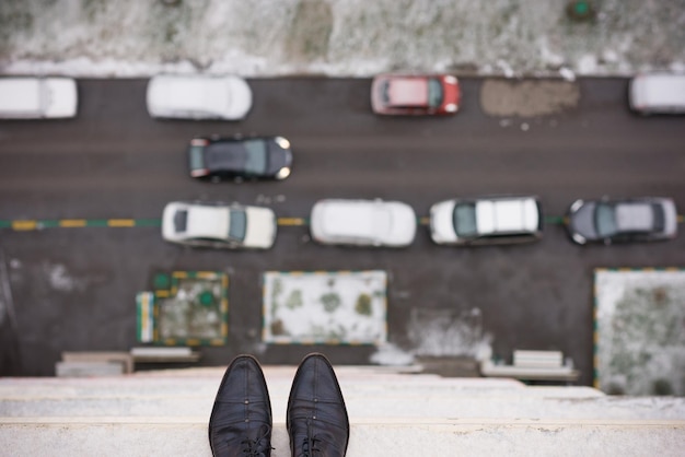 Sapatos do homem em pé na beira do telhado de um prédio alto em crise de depressão e instabilidade