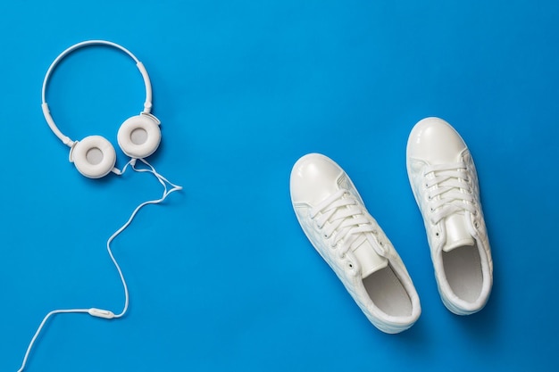 Sapatos esportivos brancos e fones de ouvido em um fundo azul brilhante O conceito de estilo de vida saudável e música