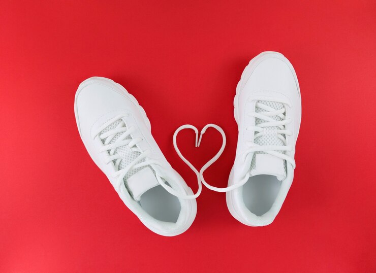 Foto sapatos esportivos brancos e forma de coração de atacadores em um piso vermelho. configuração plana simples.