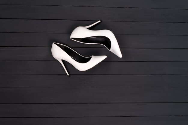 Foto sapatos femininos brancos sobre uma superfície de madeira preta