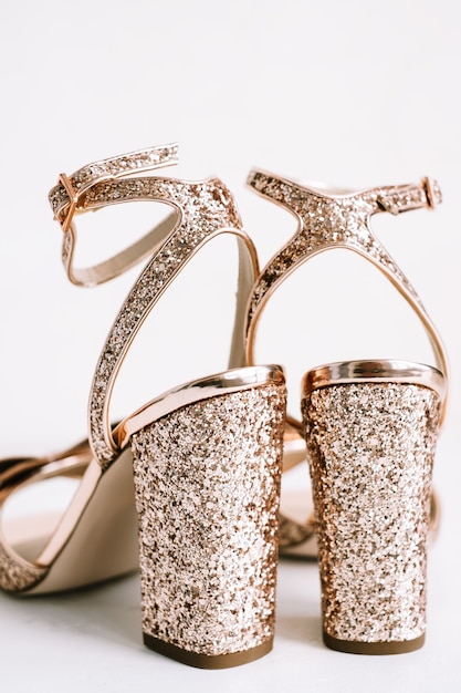 Sapatos femininos dourados com saltos e lantejoulas em fundo branco.