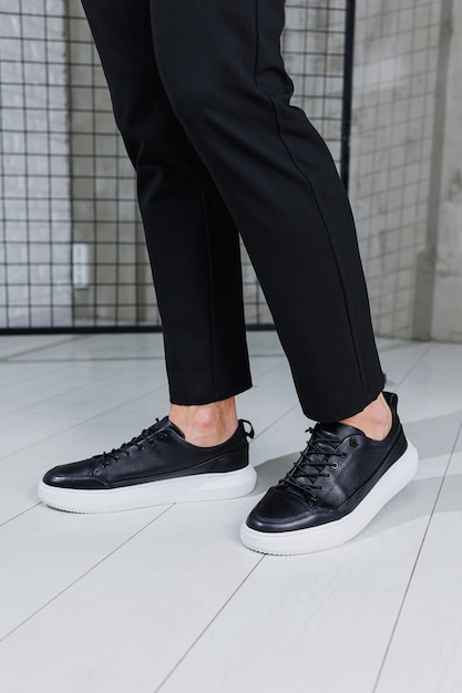 Sapatos masculinos modernos Pernas masculinas em calças pretas e tênis casuais pretos Sapatos masculinos da moda