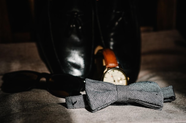Sapatos masculinos pretos lacados elegantes óculos de relógio gravata cinza para noivo Acessórios de casamento em fundo marrom rústico tradicional conceito de férias de composição de ideia silhueta sombra sol