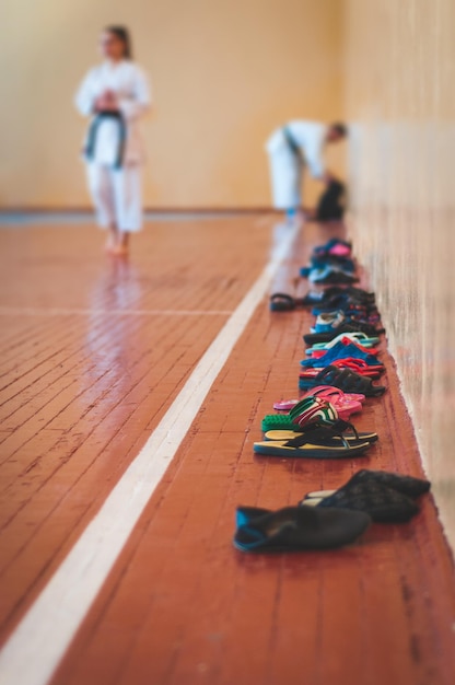 Sapatos praticados na entrada da sala de karatedo Pano de fundo de uma jovem em roupas brancas com faixa preta Para páginas da web ou impressão de publicidade Foto sem rostos