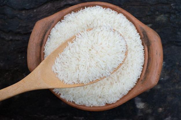 Saque el arroz usando un cucharón en una olla de barro en el fondo de madera