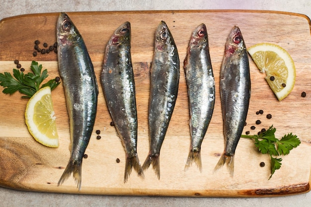 Sardinas frescas en una tabla de madera de cocina con rodajas de limón