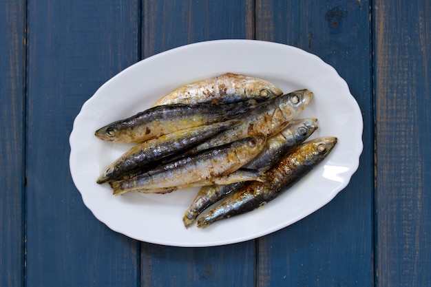 Sardinas fritas en plato blanco sobre superficie de madera azul