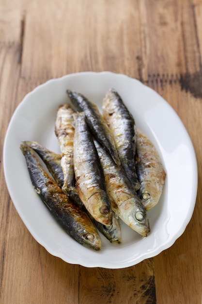 Sardinas fritas en plato blanco sobre superficie de madera marrón