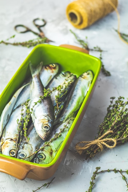 Sardinas o arenque báltico en un plato verde con tomillo en la superficie de una mesa de hormigón gris claro Pescado de mar crudo sin cocer