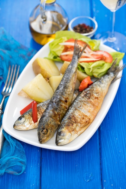 Sardinas a la plancha con patata hervida y ensalada en plato blanco