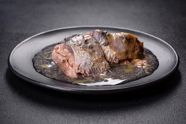 Sardinha enlatada em óleo em uma placa redonda preta contra um fundo escuro de concreto fazendo um lanche delicioso