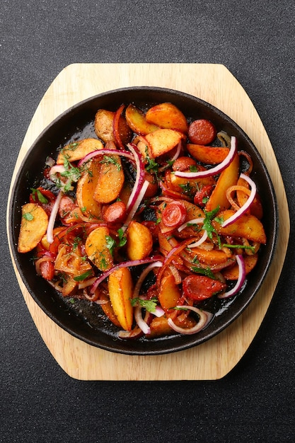 Sartén con carne de patatas y cebolla sobre fondo de hormigón negro