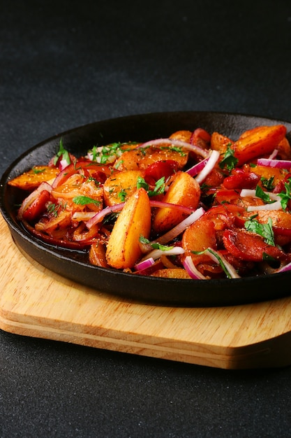 Sartén con carne de patatas y cebolla sobre fondo de hormigón negro