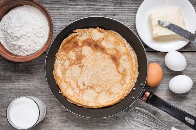 sartén con deliciosas crepes e ingredientes para cocinar en la mesa de madera rústica panqueques delgados en