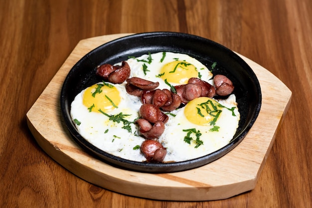 Sartén con huevos revueltos y salchicha frita adornada con perejil Sobre una tabla de madera Menú de restaurante con concepto de desayuno saludable