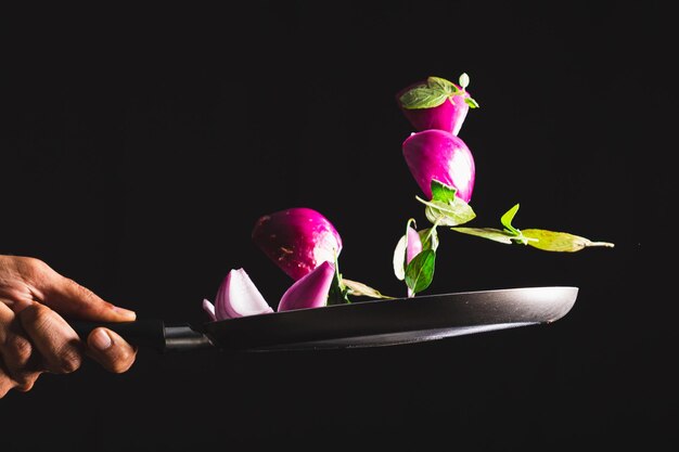 Sartén lanzando ingredientes como cebolla roja queso albahaca y condimentos en el aire