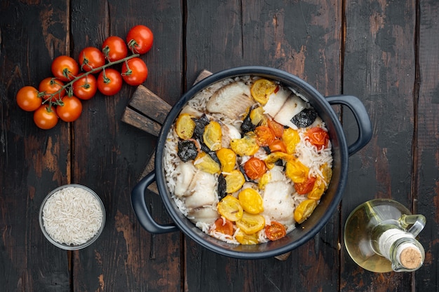 Una sartén de pescado fabuloso, con arroz basmati y tomates cherry, sobre la mesa de madera antigua, vista superior