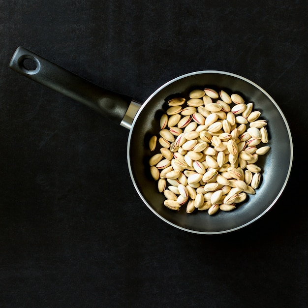 Sartén con los pistachos en un fondo negro.