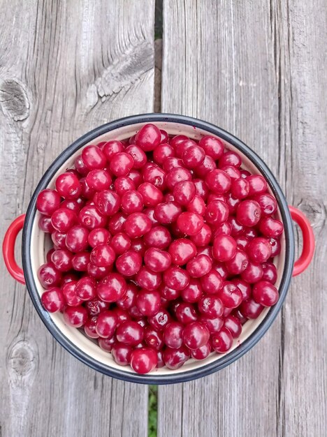 Foto una sartén roja llena de bayas maduras, jugosas y deliciosas en una vieja mesa de madera