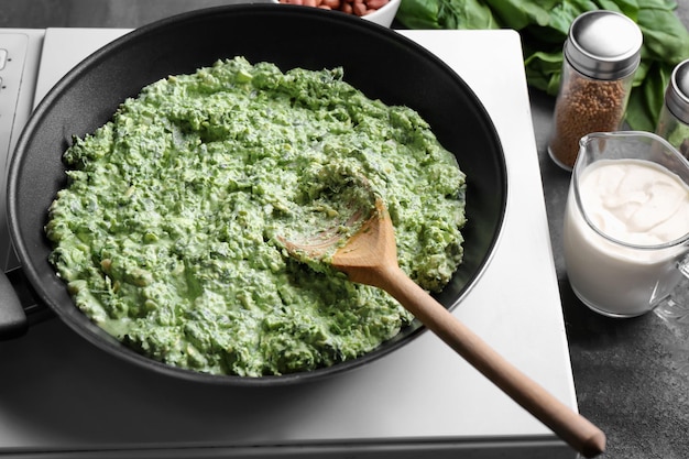 Sartén con sabrosa salsa de espinacas en cocina eléctrica en la cocina