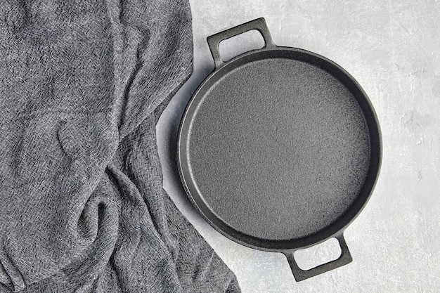 Sartén vacía de hierro fundido negro y toalla de cocina gris sobre un fondo de hormigón gris