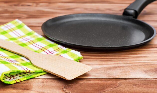 Sartén vacía con pala de madera y toalla de cocina sobre mesa de madera