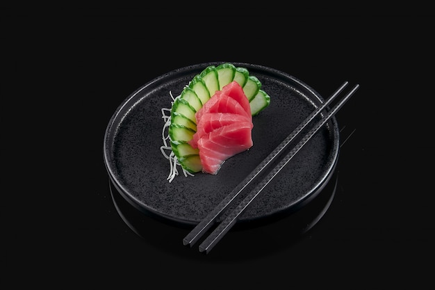 Sashimi de atún crudo clásico con rábano daicon sobre una elegante placa de cerámica negra sobre una superficie negra. Comida tradicional japonesa Foto del menú.