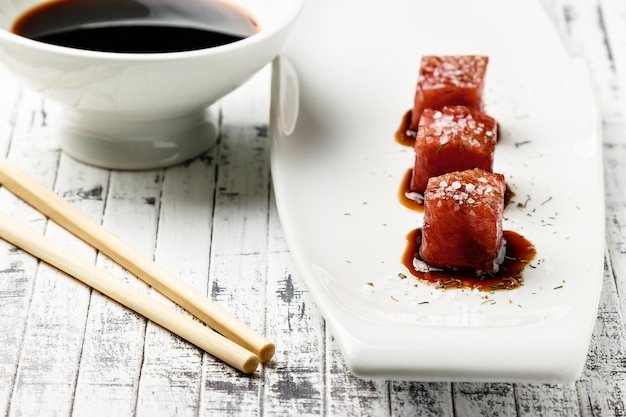 Sashimi de atún sumergido en salsa de soja, sal espesa y eneldo en una vieja tabla de madera blanca con palillos