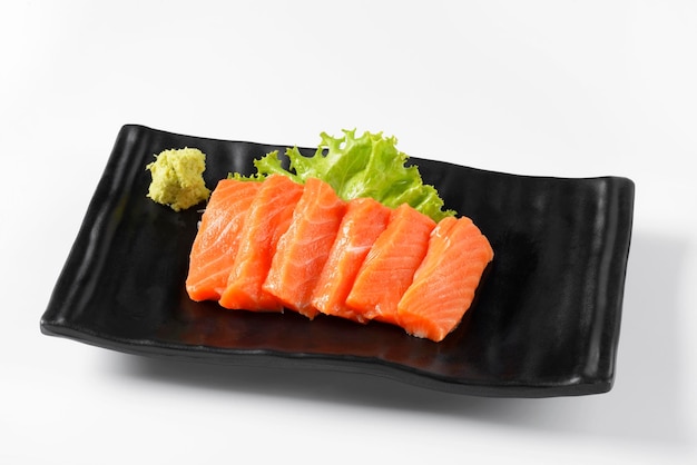 Sashimi de salmão arranjado em um prato preto com lado de wasabi. em um fundo branco