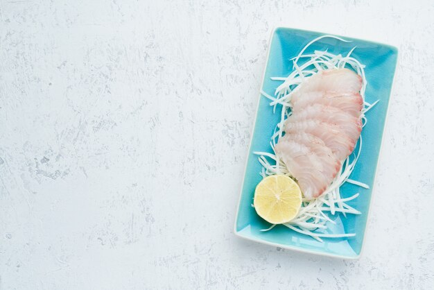 Sashimi de rodajas de filete de pescado blanco crudo en un plato azul sobre blanco