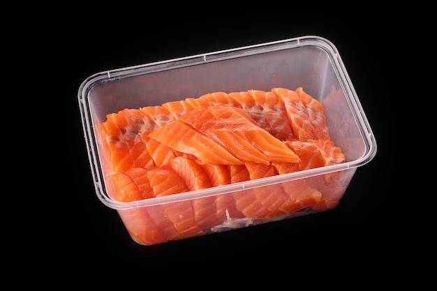 Sashimi de salmón crudo en rodajas apiladas en un recipiente de plástico para alimentos aislado en fondo negro