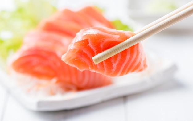 Sashimi de salmón con palillos sosteniendo un trozo de salmón en rodajas