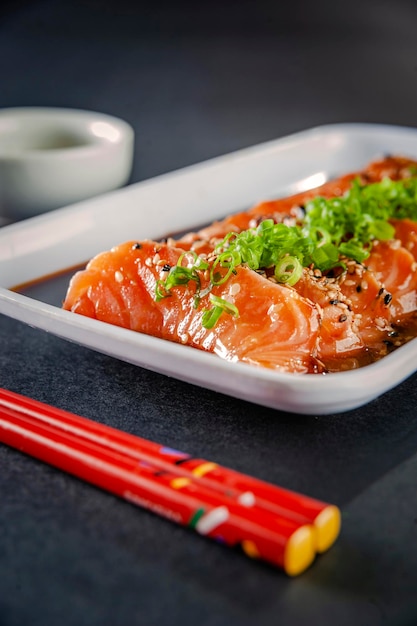 Sashimi de salmón con sésamo, shoyu, salsa miso y palillos sobre una mesa negra.