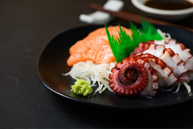 Sashimi de salmón y tako en una placa negra